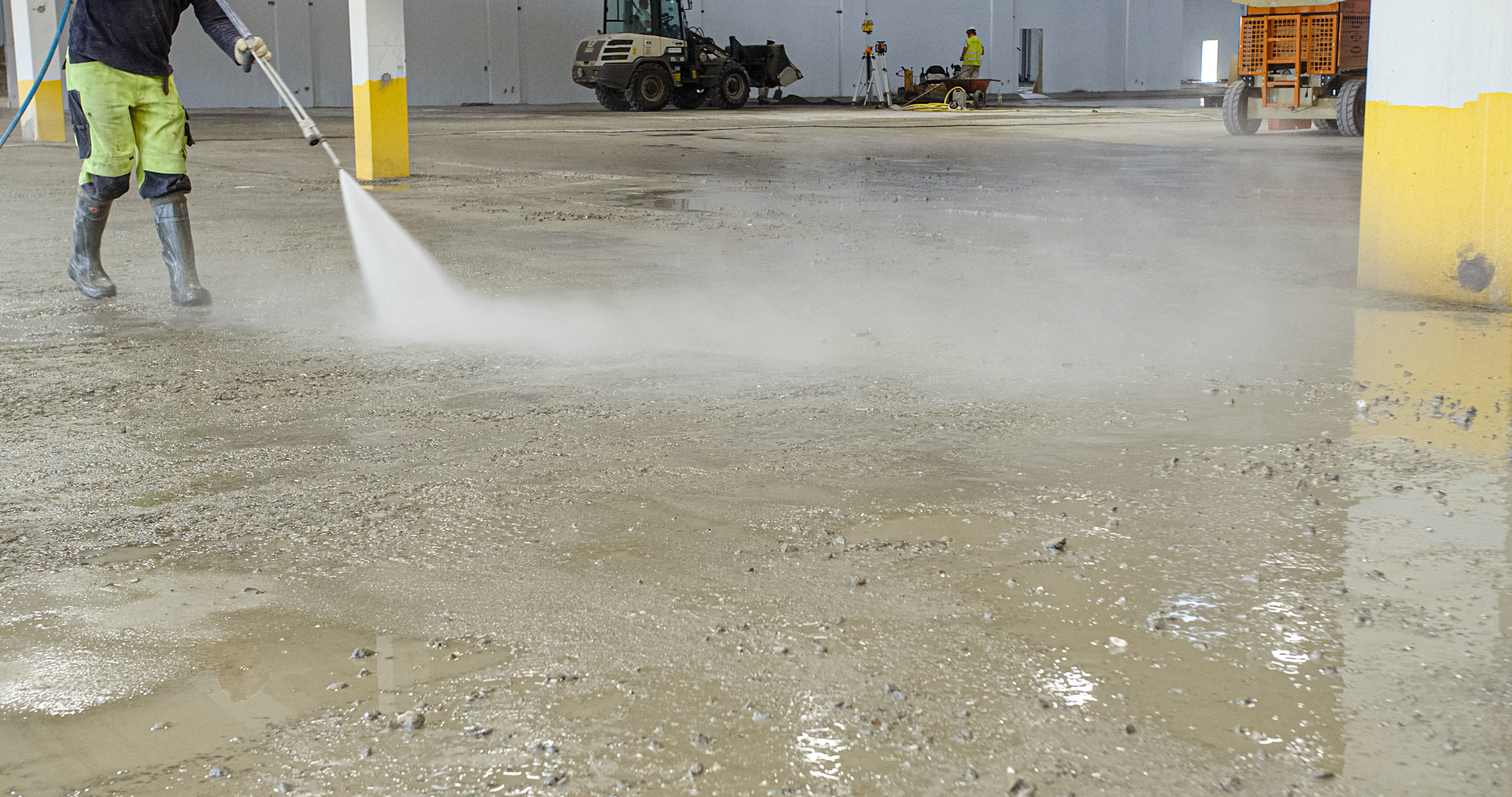 Arbetare spolar golv och förbereder för Teqplan applicering för lagergolv