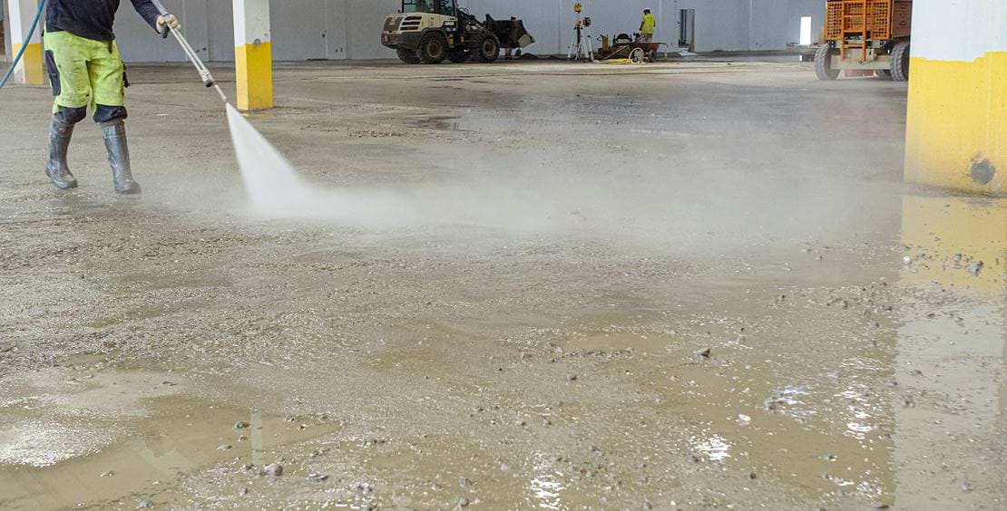 Arbetare spolar golv och förbereder för Teqplan applicering för lagergolv